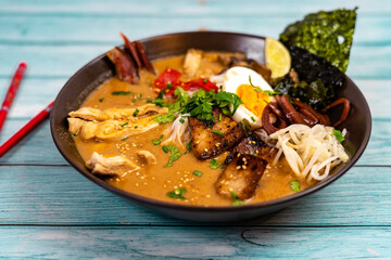 Japanese ramen soup with chicken, egg, pork, vegetables and sprouts on light wooden background
