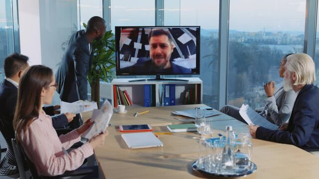 Angry Caucasian Boss Yelling at Colleagues from Distant Videochat Call. Furious African Employee Smashing Up TTV with Baseball Bat. Concept for Justice.