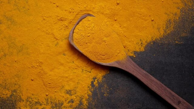 Indian spices turmeric powder in wooden spoon falling on black background, Kerala India Sri Lanka traditional Indian curry masala 4K slow motion video footage, antiseptic antiviral Ayurvedic medicine.