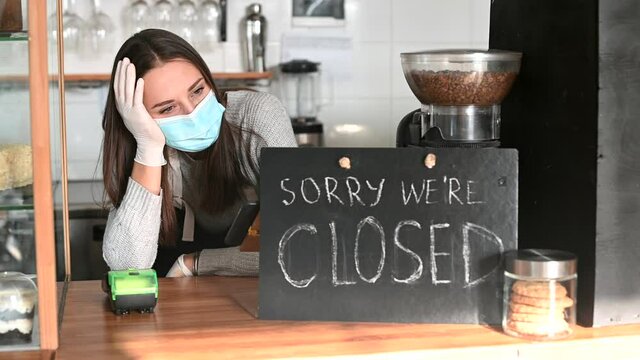 Frustrated female owner wearing medical mask leaned on bar counter in closed cafe, crisis in small business due to coronavirus lockdown, bankrout concept