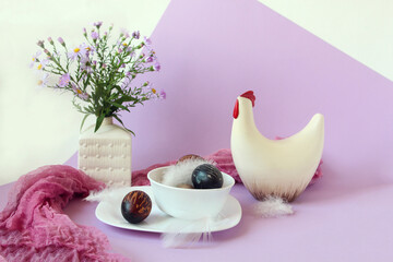 Easter eggs in a white dish with light feathers on the background of a chicken figure and a spring...