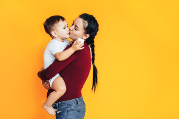 Pregnant young woman holding a small baby in front of a yellow background. Caring for the health of a pregnant woman. Artificial insemination