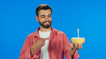 Young bearded man in a red shirt shows food in hand isolated on blue background.