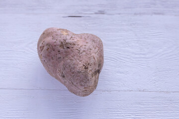 An ugly heart-shaped potato on a wooden background. Funny, crazy Concept of Plant or food waste