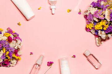 Top-view layout shot with beauty goods and flowers surrounding the copy space on a pastel pink...
