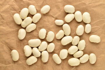 Fototapeta na wymiar Several dried grains of organic white beans on brown paper, top view.