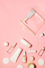 Vertical flat lay shot with skincare goods: shampoo, deodorant, cream, facial mist, essence, serum, lipstick, balm, cotton pads and buds with a candle on a pastel pink background.