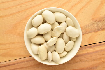 Dried grains of organic white beans in a ceramic bowl on a wooden table, top view.
