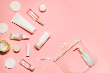 Top view flat lay with skincare goods: shampoo, deodorant, cream, facial mist, essence, serum, lipstick, balm, cotton pads and buds on a pastel pink background.