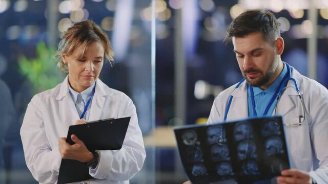Professional doctor and niurse discussing MRI scanning image of disabled patient making diagnosis writing medical report. Healthcare. Hospitals.