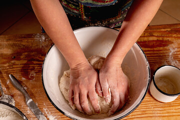 Top view of female baker prepares the dough for baking on kitchen wooden table. Selective focus on hands.