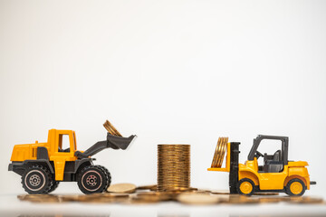 Business, Money and Financial Concept. Closeup  mini forklift and loader truck mini car toy model contain coins to stack of gold coins on white background.