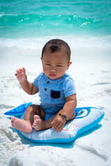 Infant in blue playing on the beach in front of the blue water