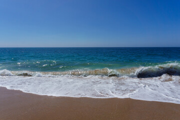 Waves washing onto sandy beach on a sunny clear day in Southern California under a clear blue sky.