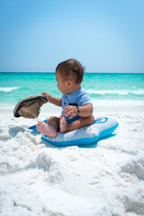 Beautiful toddler on the beach with hat and float