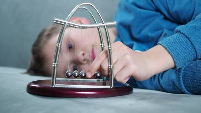 a boy plays with a Newton's pendulum balls lying on divine.