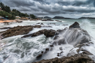 Ocean wave breaking at rocks on coastline in stormy