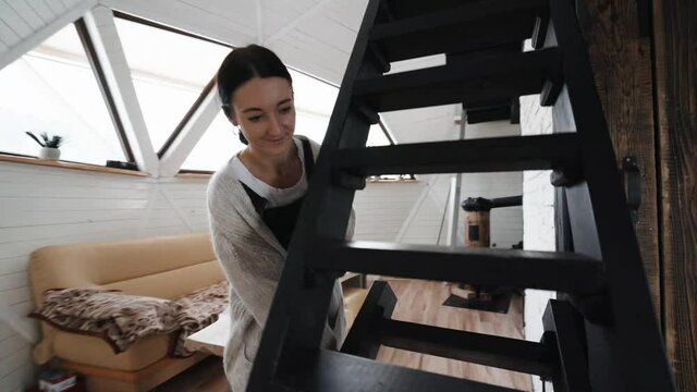 A young woman taking up the wooden stairs and going up the stairs. Showing Beautiful Tiny House, Geodesic Dome, Unusual Architecture concept.