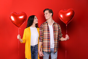 Happy Valentine's day concept. Studio shot of couple in love holding a heart shaped balloon, showing affection. 14th february - the lovers day. Red wall background, copy space, portrait, casual style.