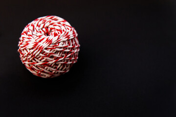 On a black background, a ball of twine is red and white. Threads for wrapping gifts.