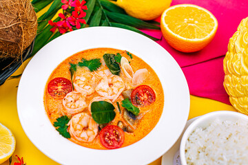 Thai soup tom yam with shrimps and tomatoes and rice as a garnish on a decorated table