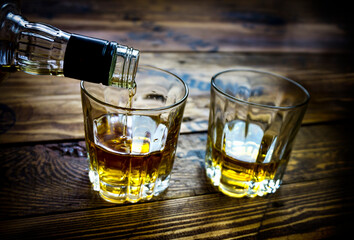 two whiskey glasses in a wooden pallet table pouring whiskey in one of them
