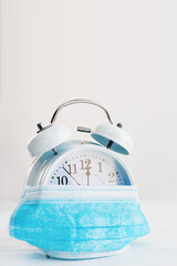 Protective mask on alarm clock as a concept for the introduction of quarantine measures with copy space vertical shot