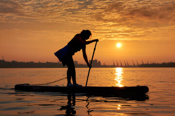 Silhouette of a young woman rowing on a SUP during a beautiful winter sunrise on the river