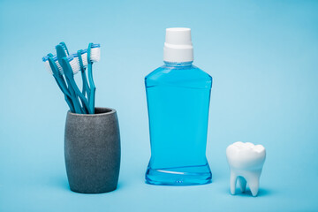 Fototapeta na wymiar Toothbrushes, mouthwash and white model of tooth on blue background