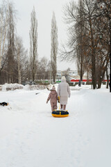 Winter entertainment and leisure in Russia. Mom walks with her daughter and snow tubing along the paths in the park.