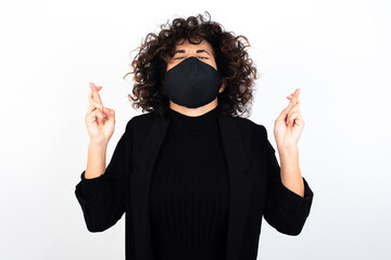 Joyful young beautiful caucasian woman wearing medical mask standing against white wall clenches...
