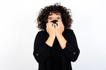 Anxiety - young beautiful caucasian woman wearing medical mask standing against white wall covering his mouth with hands scared from something or someone bitting nails.