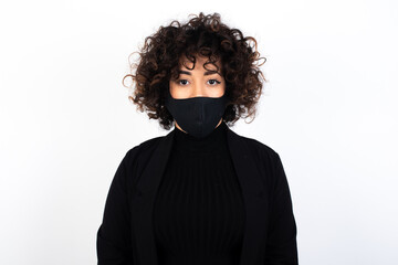 Obraz premium Joyful young beautiful caucasian woman wearing medical mask standing against white wall looking to the camera, thinking about something. Both arms down, neutral facial expression.