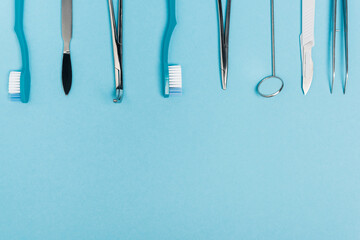 Top view of row of dental tools and toothbrushes on blue background with copy space