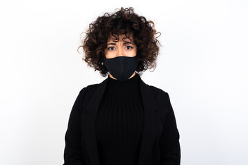 young beautiful caucasian woman wearing medical mask standing against white wall, frowning his eyebrows being displeased with something.