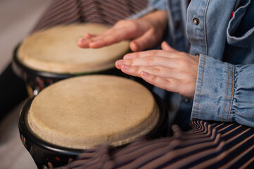 Close-up of female hands on mini bongo drums. The girl plays a traditional ethnic percussion instrument