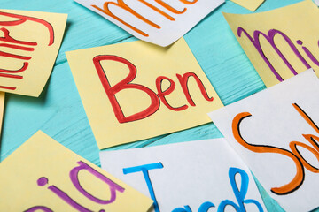 Paper notes with different baby names on light blue wooden table, closeup