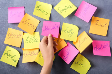 Woman taking paper note with baby name from grey wall, closeup