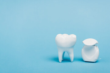 White tooth model and dental floss on blue background with copy space