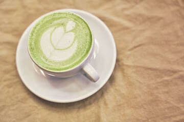 Cup of matcha latte on wooden background and napkin in a cafe with copy space
