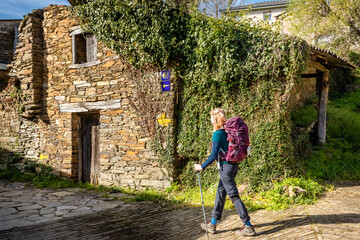 Pilgrim Girl Walking in Town of Triacastela Galicia Spain along the Way of St James Camino de Santiago Pilgrimage Trail - obrazy, fototapety, plakaty