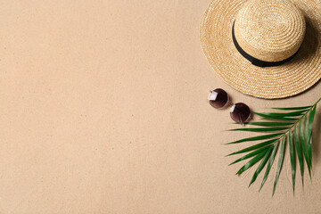 Straw hat, sunglasses, palm leaf and space for text on beach sand, flat lay. Summer vacation
