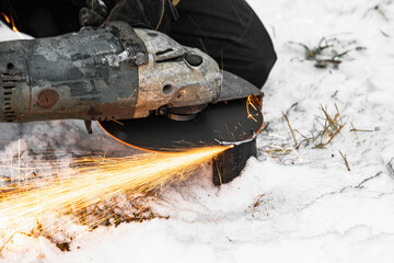 Angle grinder works with sparks over white snow