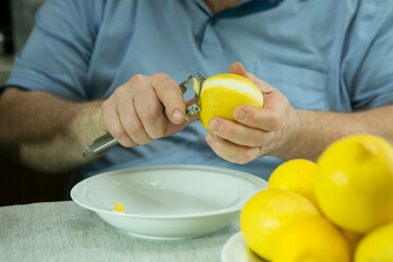 The process of making limoncello lemon liqueur at home. The man removes the zest from the lemons.