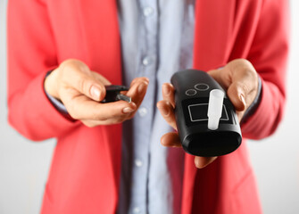 Woman holding modern breathalyzer and car key on light background, closeup
