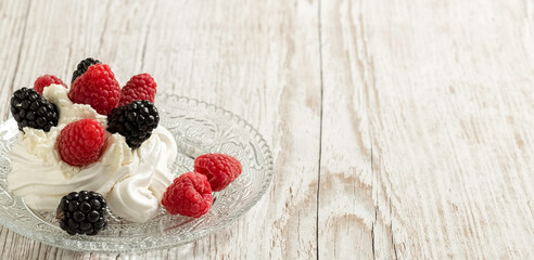 Pavlova's cake, decorated with raspberries and blackberries. Light wooden background. Home cooking. Banner.