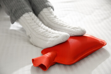 Person warming feet with hot water bottle on bed, closeup