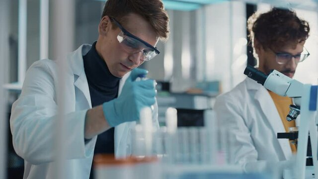 Modern Medical Research Laboratory: Portrait of Two Young Scientists Using Pipette, Digital Tablet, Doing Sample Analysis, Talking. Diverse Team of Specialists work in Advanced Bio Technology Lab