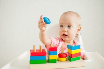 little girl plays with an educational toy - a multi-colored wooden pyramid. Development of fine motor skills and logical thinking. High quality photo