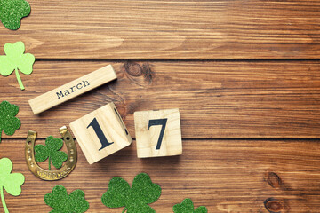 Decorative clover leaves, horseshoe and block calendar on wooden background, flat lay with space for text. St. Patrick's Day celebration